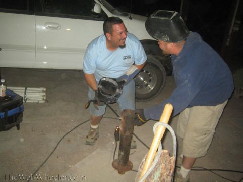 1990 Ford Bronco - Two men share a laugh while working on a rusty metal post at night, one in a welding mask, beside a white truck.