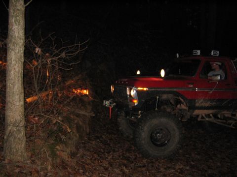 1979 Ford Bronco - A red SUV with off-road modifications navigates a wooded trail after dark.