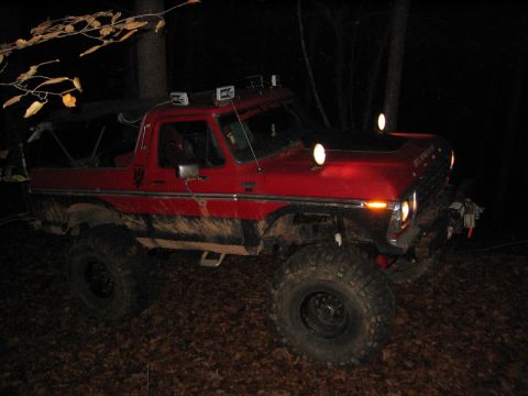 1979 Ford Bronco - A red 1979 Ford Bronco is shown off-road at night, equipped with large tires and auxiliary lighting.