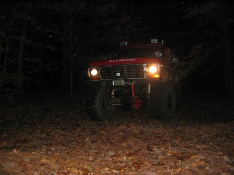 1979 Ford Bronco - This lifted truck is ready for off-road adventures, illuminated by its headlights in a dark, wooded area.