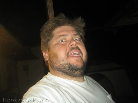 1990 Ford Bronco - bearded man in a white t-shirt mugs a wide-eyed, open-mouthed expression close to the camera at night.