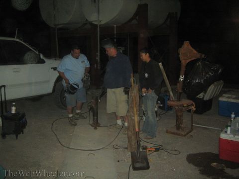1990 Ford Bronco - Three people work on rusty metal posts at night under elevated tanks, with a white truck and coolers nearby.