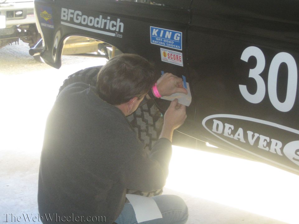 Man kneeling to apply a decal to a black off-road race truck door numbered 30
