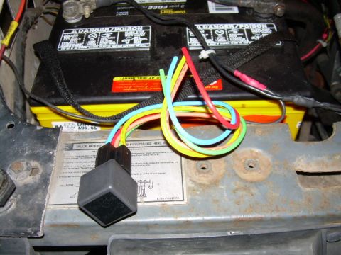 1988 Ford Bronco - Close-up of a car battery and its wiring harness, including a relay.
