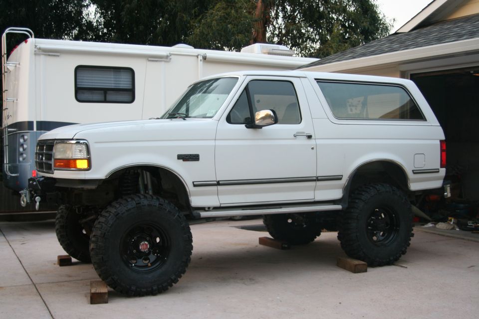 1992 Ford Bronco with lifted suspension and large off-road tires parked next to an RV