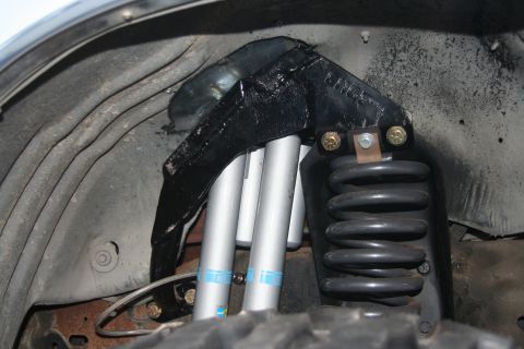 1992 Ford Bronco - Close-up of a modified front suspension system dual shocks and a heavy-duty coil spring, with "SUPERMOTORS" branding visible.