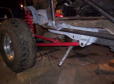 1984 Ford Bronco - The chassis of a modified off-road vehicle is shown with a large tire and red suspension components.