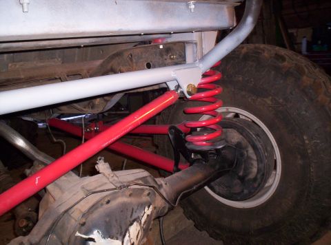 1984 Ford Bronco - Close-up of a vehicle's modified rear suspension system, red shocks and springs.