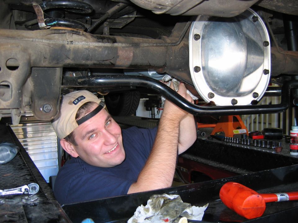 Man in tan baseball cap working on a car's rear differential with a shiny cover