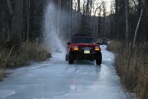 2003 Jeep TJ - Two Jeep Cherokees drive through a partially frozen, watery path surrounded by trees.