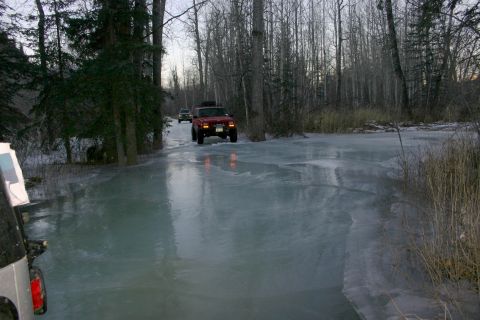 2003 Jeep TJ - A red Jeep Wrangler navigates a frozen road through a wooded area, with another vehicle following behind.
