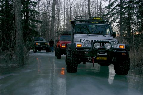 2003 Jeep TJ - Three SUVs drive on a frozen surface surrounded by trees.