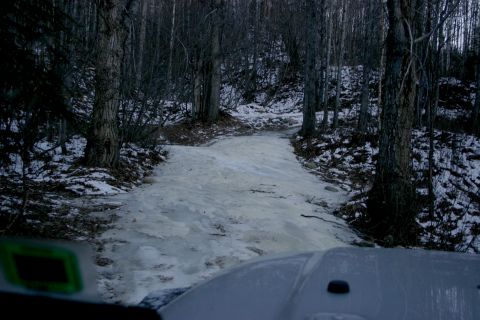 2003 Jeep TJ - View from inside a white Jeep driving on a partially frozen road through a wooded area.