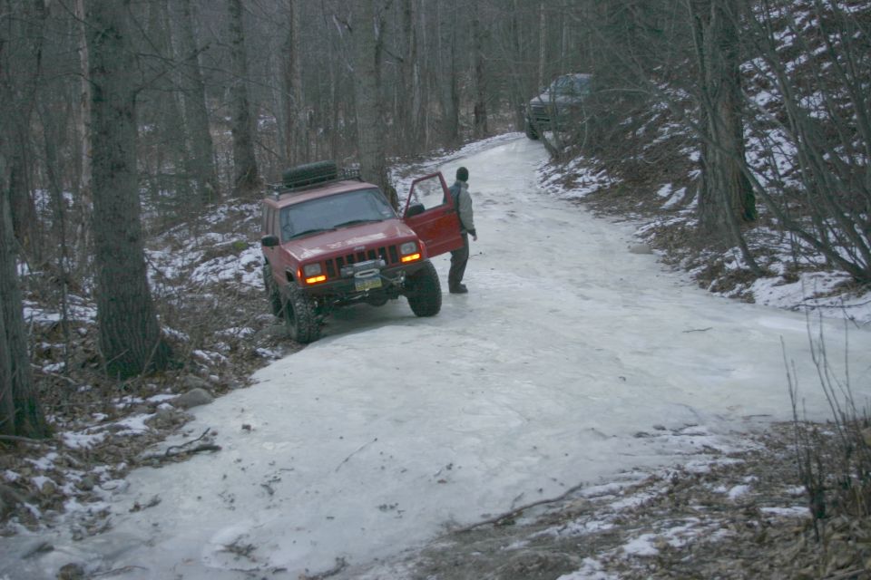 Red 2003 Jeep TJ on icy road with door open, another vehicle behind