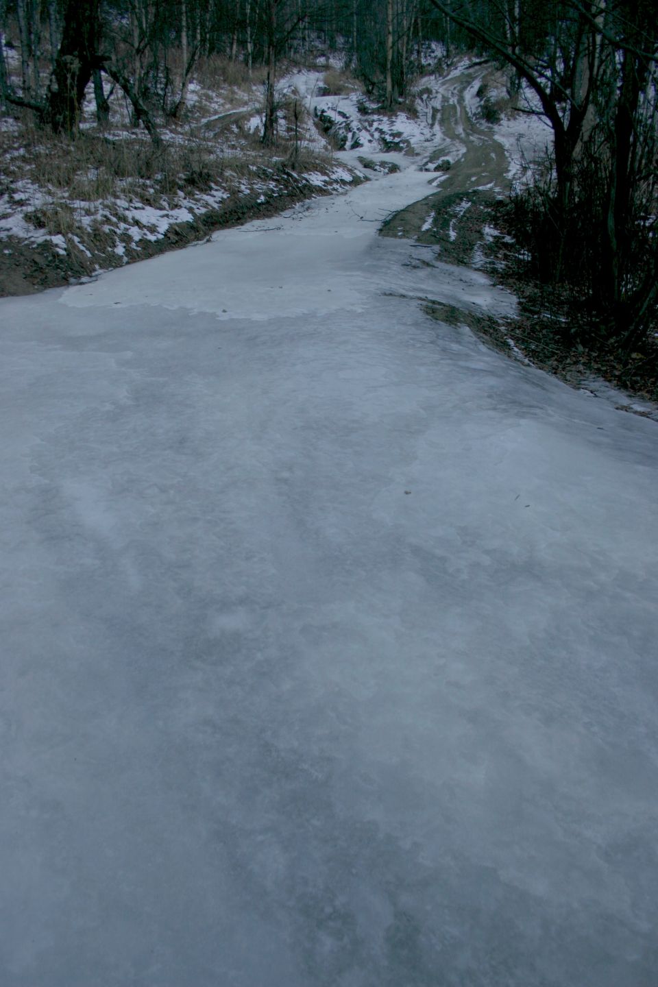 Icy road winding through a bare, wooded landscape with snow on the ground