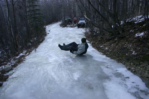 2003 Jeep TJ - A person slides down a frozen road in a wooded area, with several SUVs visible further up the path.