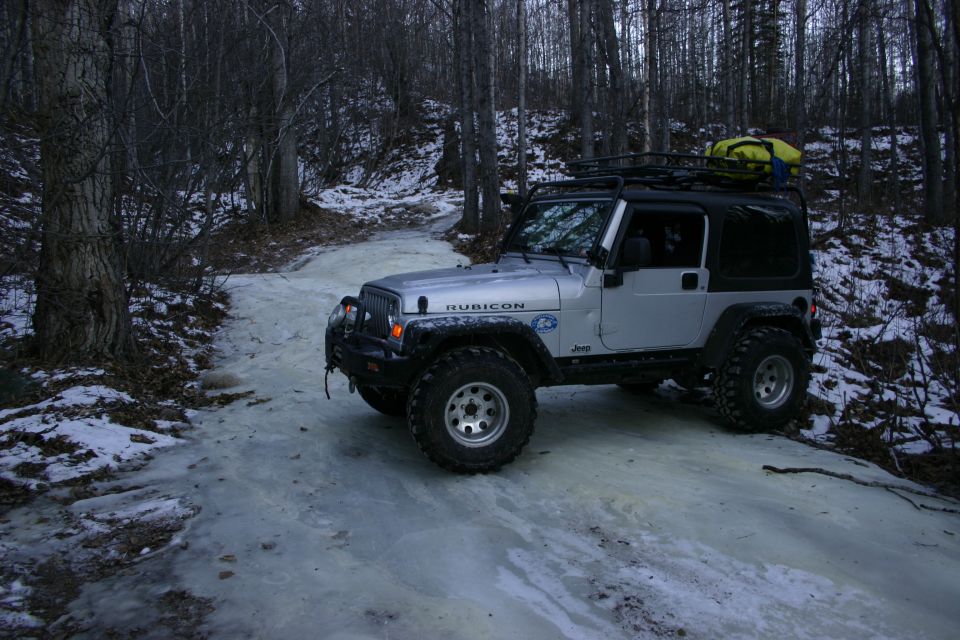 Silver 2003 Jeep TJ Rubicon with roof rack and yellow bag on icy forest road