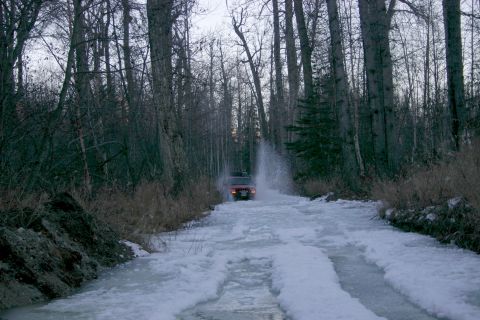 2003 Jeep TJ - A red 2003 Jeep TJ splashes through an icy road surrounded by a winter forest.