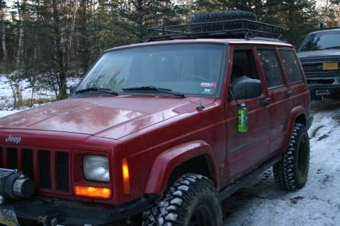 2003 Jeep TJ - A red Jeep Cherokee is parked in a snowy, wooded area with another vehicle behind it.