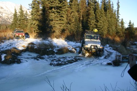 2003 Jeep TJ - Two Jeep Wranglers navigate an icy trail with snow-covered trees and mountains.