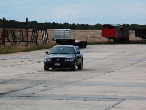 2001 Mercury Grand Marquis - A dark sedan is captured from the front as it drives on a paved surface under a cloudy sky.