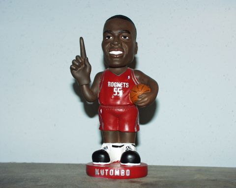2000 Ford Crown Victoria - A Dikembe Mutombo bobblehead doll stands on a red base with his name on it.
