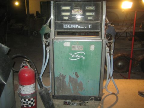 1990 Ford Bronco - vintage green Bennett gas pump stands in a dim garage beside a red fire extinguisher and hanging fuel hoses.