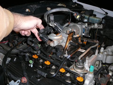 1997 Mercury Grand Marquis - Under-hood close-up of a fuel-injected V8 with the injector area exposed, showing orange-topped fuel injectors seated in the rail, a metal…
