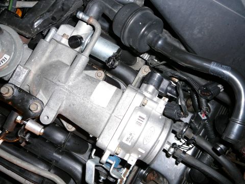 1997 Mercury Grand Marquis - Close-up down onto the cast aluminum upper intake elbow and throttle body in an engine bay, with the Ford oval and part label on the thrott…