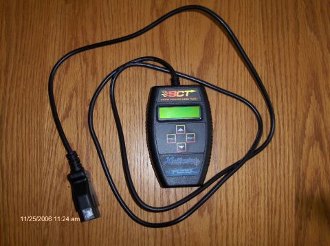 2004 Ford Crown Victoria - A black SCT handheld tuner with a green display and navigation buttons lies on a wooden surface next to its diagnostic cable.