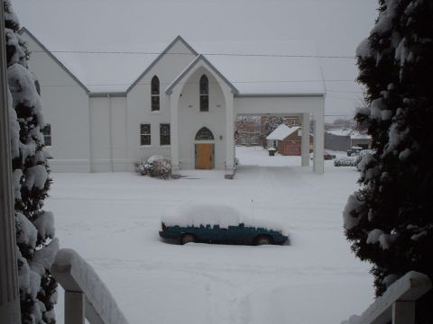 1990 Ford Bronco - A car is buried in snow in front of a church during a winter storm.
