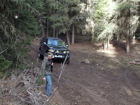 1990 Ford Bronco - A black SUV navigates a muddy trail through a wooded area, with a person walking nearby.