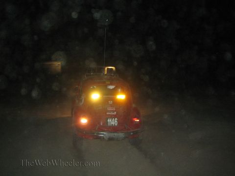 1990 Ford Bronco - red Volkswagen Beetle off-road race car numbered 1146 drives away on a dark dusty course with tail lights and roof lights glowing.