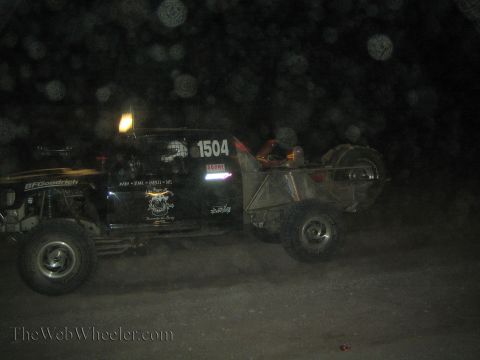 1990 Ford Bronco - black off-road race buggy numbered 1504 with BFGoodrich decals kicks up dust as it moves along a dark course at night.
