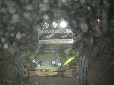 1990 Ford Bronco - Front view of a green off-road buggy numbered 1409 with bright roof and head lights cutting through dusty night air.