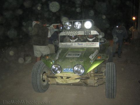 1990 Ford Bronco - Several people gather around a green off-road buggy numbered 1409 with roof lights glowing in a dusty nighttime scene.