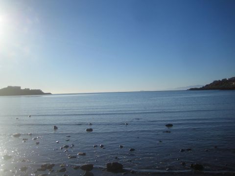 1990 Ford Bronco - Scattered rocks dot the shallows of a calm blue bay backed by a rocky point under a bright clear sky.