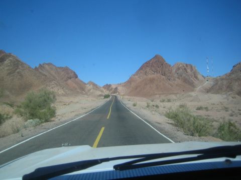 1990 Ford Bronco - two-lane highway heads straight toward a sharp pyramid-shaped reddish rock peak amid arid desert terrain.