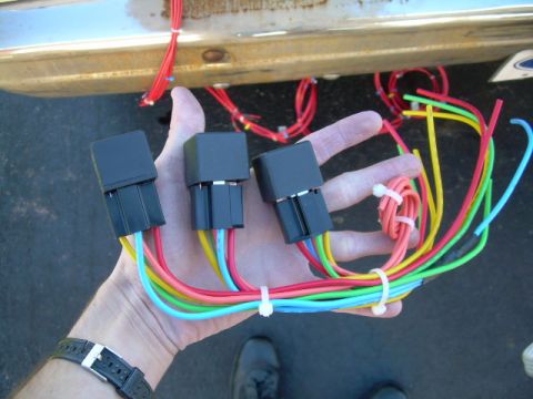 1988 Ford Bronco - Wiring harnesses and relays are held in a hand, with a vehicle's bumper visible in the background.