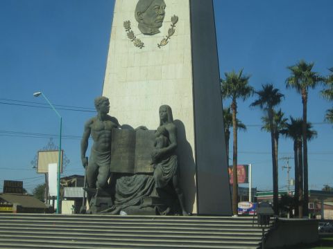 1990 Ford Bronco - tall stone obelisk monument bearing a portrait relief and sculpted standing and seated figures stands among palm trees in a city.