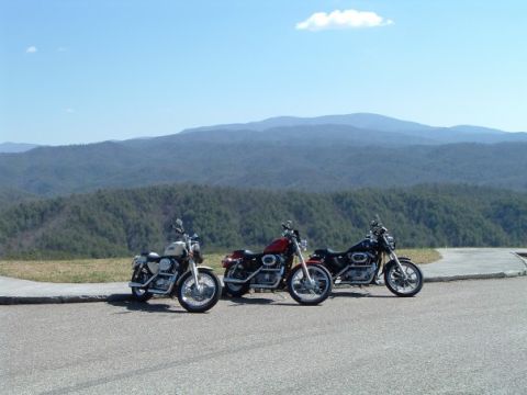 2002 Harley-Davidson Sportster Custom - Three motorcycles are parked on a paved area with a mountainous landscape behind them under a clear blue sky.