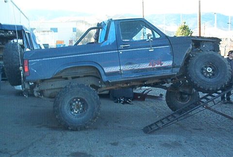 1986 Ford Bronco - A modified blue SUV is positioned on a metal ramp, with a spare tire mounted at the rear.