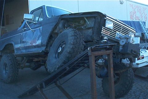 1986 Ford Bronco - A dark blue Ford Bronco with a lifted suspension and large tires is positioned on a metal ramp.