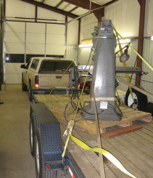 Tan pickup in a metal shop with a long gray tank strapped in the bed with yellow straps