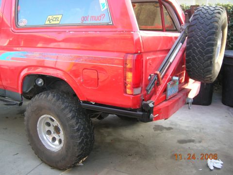 1985 Ford Bronco - Rear view of a red SUV with a spare tire mounted on the back, showing custom modifications and stickers.