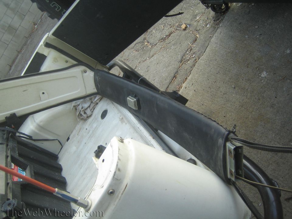 Close-up of a black plastic trim piece with a silver square latch, mounted above white vehicle interior components