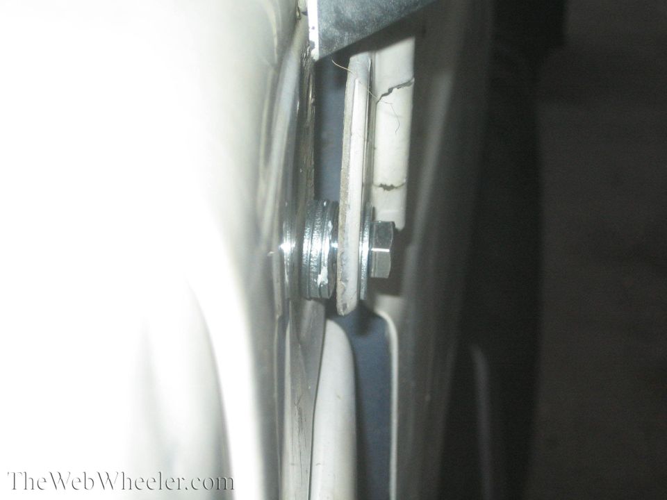 Close-up of a bolt, washers, and a metal bracket attached to a white surface