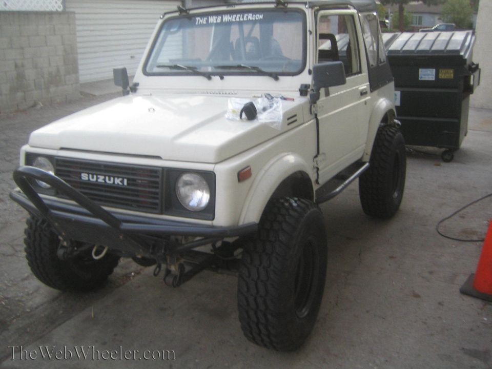 White Suzuki Samurai with off-road tires and a custom bumper parked next to a dumpster