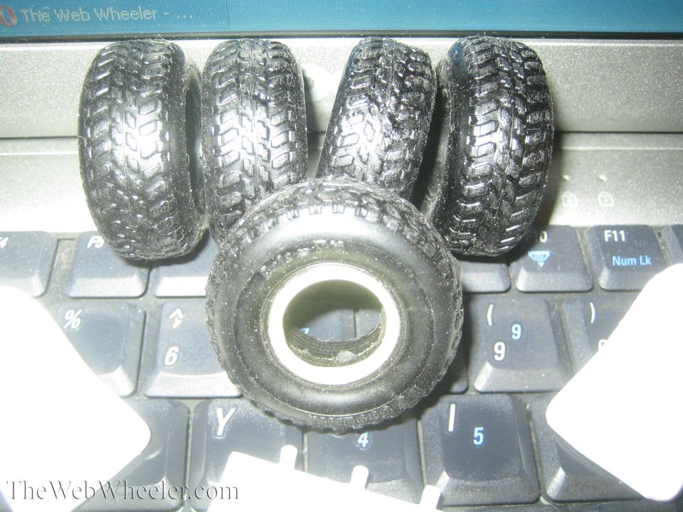 Four black toy tires with aggressive tread patterns piled on a laptop keyboard