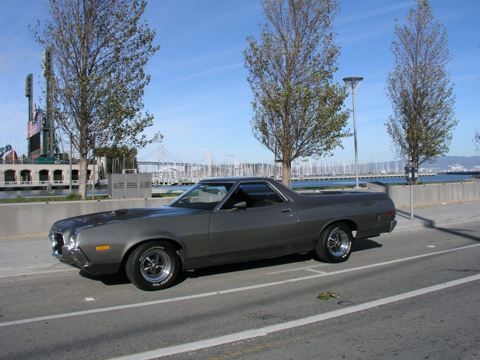 Gray 1972 Ford Ranchero parked by a waterfront with stadium in background